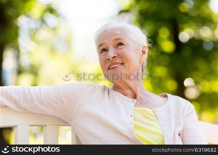 old age, retirement and people concept - happy senior woman sitting on bench at summer park. happy senior woman sitting on bench at summer park