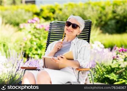 old age, retirement and people concept - happy senior woman with diary sitting in chair at summer garden. happy senior woman with diary at summer garden