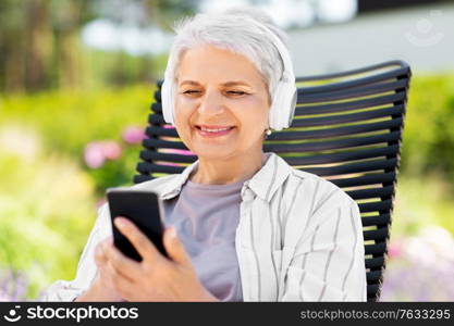 old age, retirement and people concept - happy senior woman with headphones and smartphone listening to music at summer garden. old woman with headphones and smartphone at garden