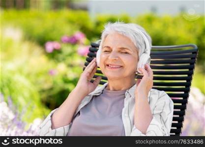 old age, retirement and people concept - happy senior woman with headphones listening to music at summer garden. happy senior woman with headphones at garden