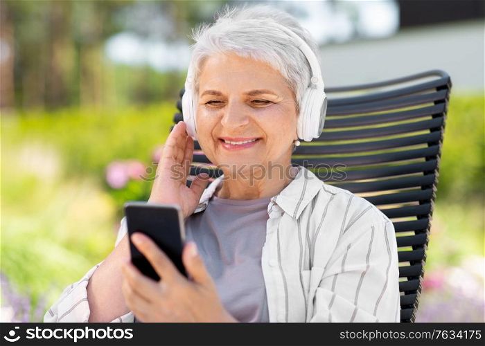 old age, retirement and people concept - happy senior woman with headphones and smartphone listening to music at summer garden. old woman with headphones and smartphone at garden