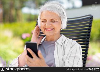 old age, retirement and people concept - happy senior woman with headphones and smartphone listening to music at summer garden. old woman with headphones and smartphone at garden