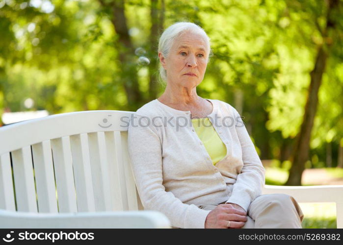 old age, retirement and people concept - sad senior woman in glasses sitting on bench at summer park. sad senior woman sitting on bench at summer park