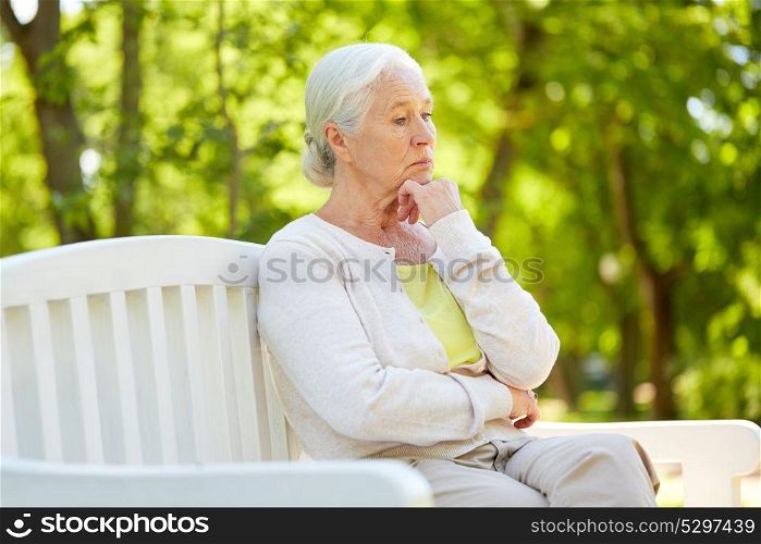 old age, retirement and people concept - sad senior woman in glasses sitting on bench at summer park. sad senior woman sitting on bench at summer park