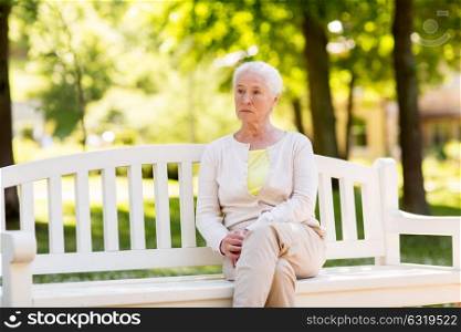 old age, retirement and people concept - sad senior woman sitting on bench at summer park. sad senior woman sitting on bench at summer park