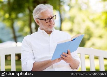 old age, retirement and people concept - senior man reading book sitting on bench at summer park. senior man reading book at summer park