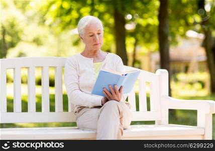 old age, retirement and people concept - senior woman reading book sitting on bench at summer park. senior woman reading book at summer park