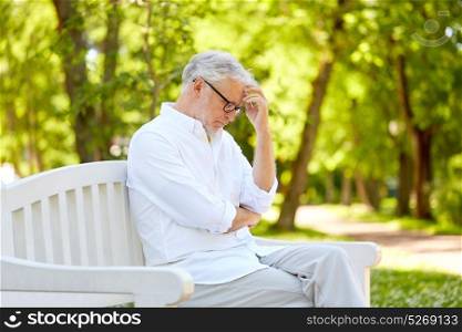 old age, retirement and people concept - thoughtful senior man in glasses sitting on bench at summer park. thoughtful senior man sitting at summer park