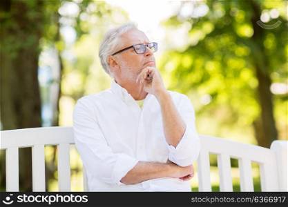 old age, retirement and people concept - thoughtful senior man in glasses sitting on bench at summer park. thoughtful senior man at summer park
