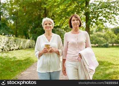 old age, retirement and people concept - two senior women or friends drinking coffee walking along summer park. senior women or friends drinking coffee at park