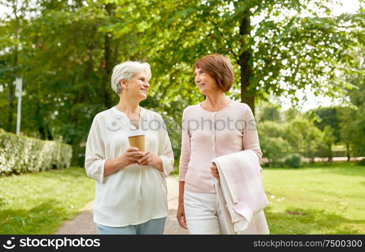 old age, retirement and people concept - two senior women or friends drinking coffee, walking and talking at park. senior women or friends drinking coffee at park