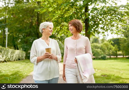 old age, retirement and people concept - two senior women or friends drinking coffee, walking and talking at park. senior women or friends drinking coffee at park