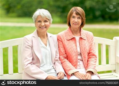 old age, retirement and people concept - two senior women or friends sitting on bench at summer park. senior women or friends sitting on bench at park