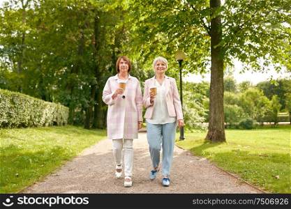 old age, retirement and people concept - two senior women or friends drinking coffee walking along summer park. senior women or friends drinking coffee at park