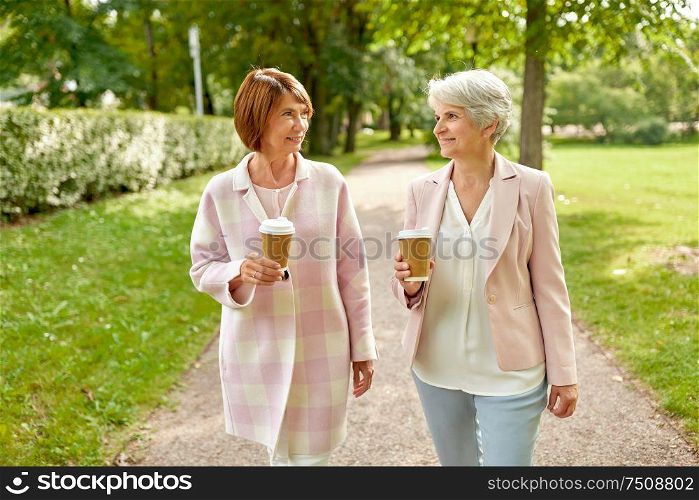 old age, retirement and people concept - two senior women or friends drinking coffee, walking and talking at park. senior women or friends drinking coffee at park