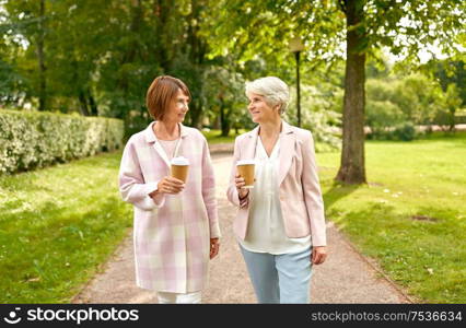 old age, retirement and people concept - two senior women or friends drinking coffee, walking and talking at park. senior women or friends drinking coffee at park