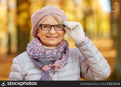 old age, retirement and season concept - portrait of happy senior woman in glasses at autumn park. portrait of happy senior woman at autumn park