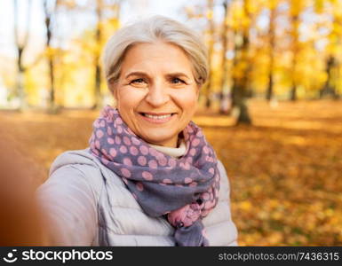 old age, retirement and technology concept - happy senior woman taking selfie at autumn park. senior woman taking selfie at autumn park