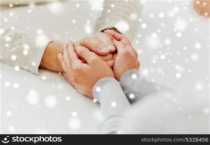 old age, support, charity, care and people concept - close up of senior man and young woman holding hands over snow. close up of old man and young woman holding hands
