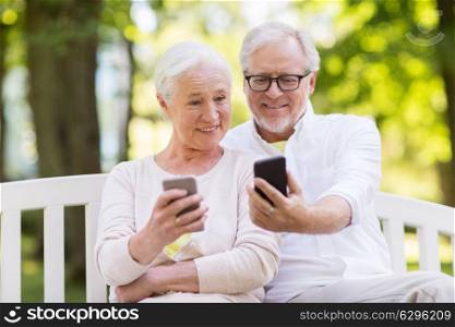 old age, technology and people concept - happy senior couple with smartphones at summer park. happy senior couple with smartphones at park
