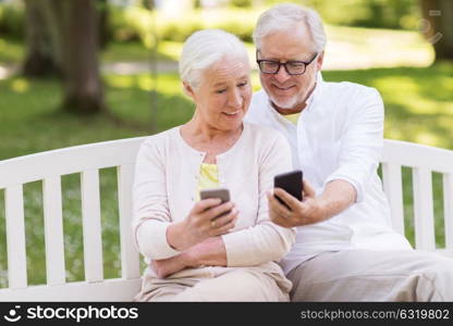 old age, technology and people concept - happy senior couple with smartphones at summer park. happy senior couple with smartphones at park