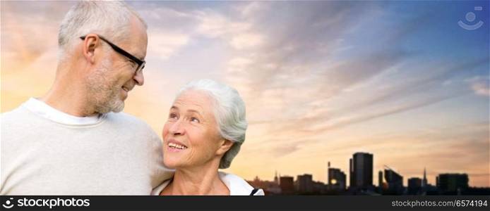 old age, tourism, travel and people concept - happy senior couple hugging over tallinn city and evening sky background. senior couple hugging over evening tallinn city
