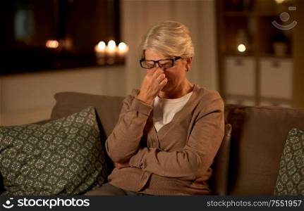 old age, vision and people concept - tired senior woman in glasses rubbing her eyes at home at night. tired senior woman in glasses at home at night