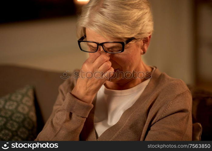 old age, vision and people concept - tired senior woman in glasses rubbing her eyes at home at night. tired senior woman in glasses at home at night