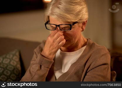 old age, vision and people concept - tired senior woman in glasses rubbing her eyes at home at night. tired senior woman in glasses at home at night