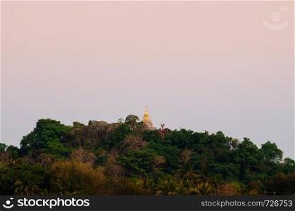 Old aged Buddhist historic Phousi Pagoda on mountain top with lush green forest in Luang Prabang, Laos under evening sky