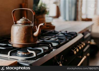 Old aluminium kettle boilng on gas stove in kitchen against cozy blurred background. Antique item made of copper metal. Vintage style