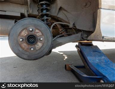 Old and dirty car without wheel, car lift up by hydraulic jack for tire repaired, close up on disc break