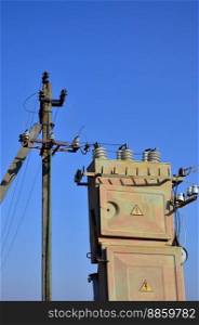 Old and obsolete electrical transformer against the background of a cloudless blue sky. Device for distribution of supply of high-voltage energy