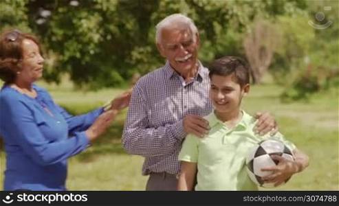 Old and young people leisure, seniors and kids in family, generations with child and retired persons. Sport activity, child playing football game, soccer in park. Happy elderly man, woman, boy smiling