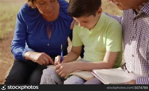 Old and young people together, seniors and children in family relationship, generations with child and elderly persons. Grandfather and grandmother helping boy with school homework, studying with book