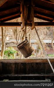 Old antique Water well wooden bucket with rope hanging above the hole