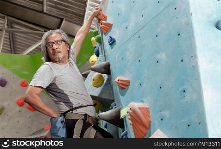 Old Asian man climbing rock mountain for adventure and sport. Activity and Retirement Concept.