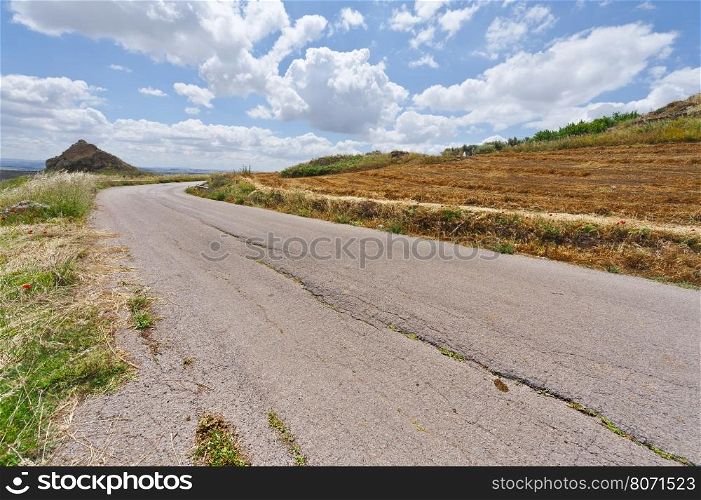 Old Asphalt Road between Mown Wheat Field in Sicily