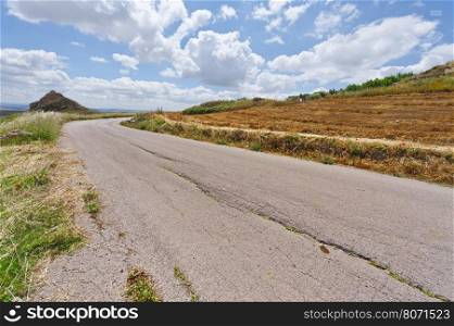 Old Asphalt Road between Mown Wheat Field in Sicily