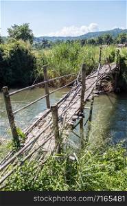 Old bamboo bridge is crossing the small river near the paddy field of the local farmer.