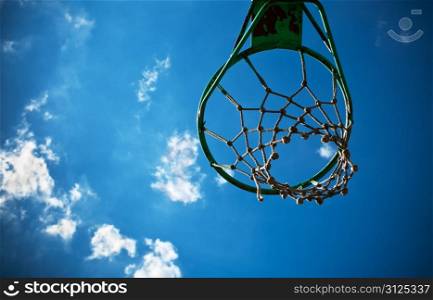 Old basketball basket with a cloudy blue sky in the background.