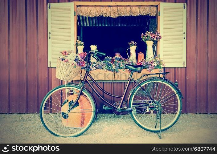 Old bicycle and flowers parked near window of farmhouse at countryside in vintage style