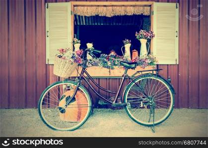 Old bicycle and flowers parked near window of farmhouse at countryside in vintage style
