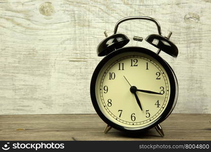 Old black alarm clock standing on a wooden countertop in a vintage style.Close horizontal view.