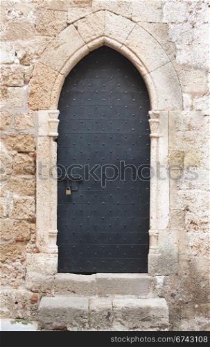 Old black wooden medieval door on limestone wall with antique sliding door bolt and padlock.