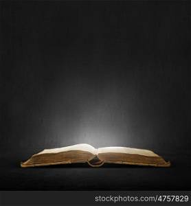 Old book in darkness. Opened book with light on pages on black background