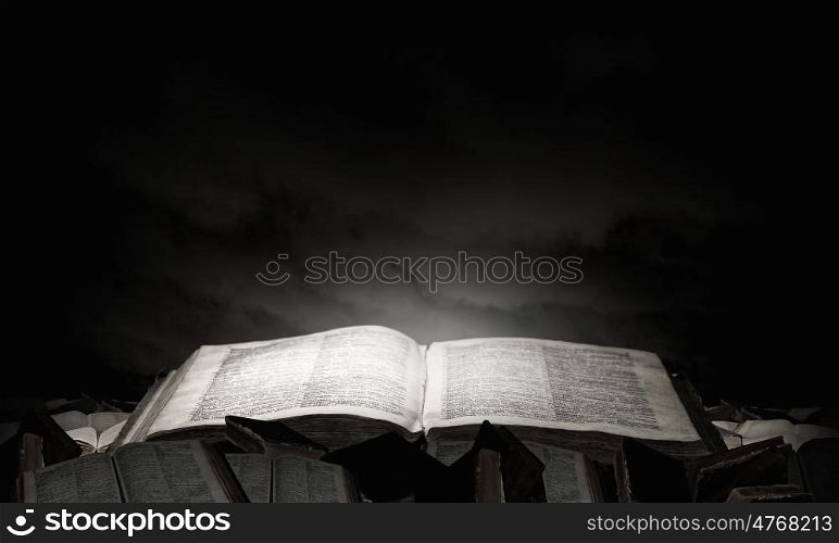Old book in darkness. Opened book with light on pages on black background