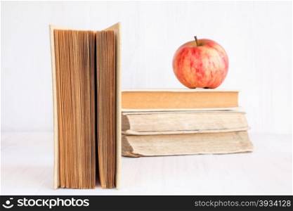 Old books and apple on white wooden bookshelf