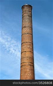 Old brick chimney. Defunct industrial brick chimney against bright blue sky