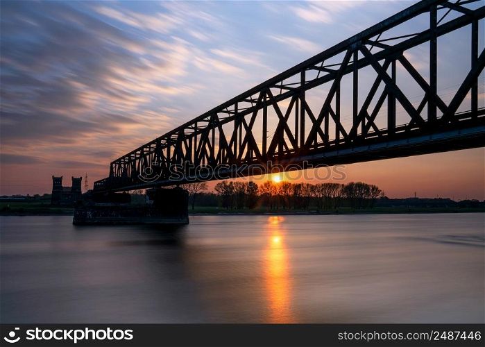 Old bridge crossing the Rhine river, sunset at Rhinepark, Duisburg, Germany